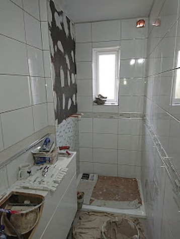 Bathroom mid-installation showing precise wall tiling around a window and shower tray